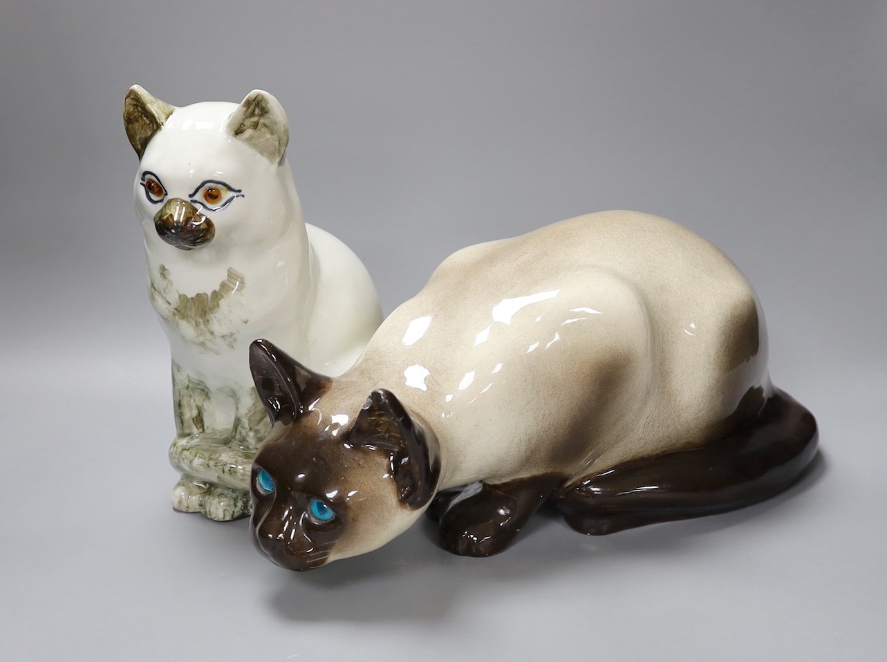 A Kensington ceramic lurking Siamese cat with blue glass eyes by Winstanley, together with another, tallest 26cm